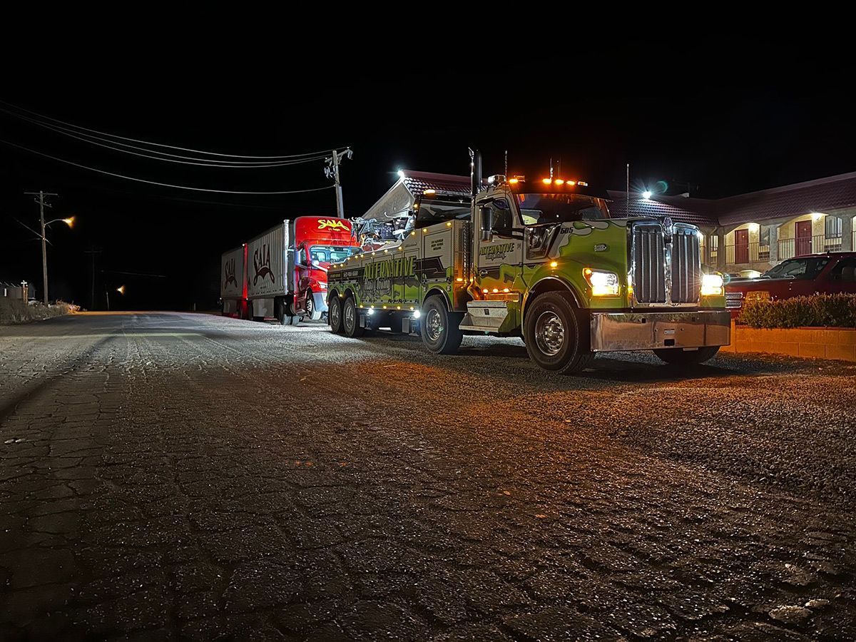 Two tow trucks are parked on the side of the road at night.
