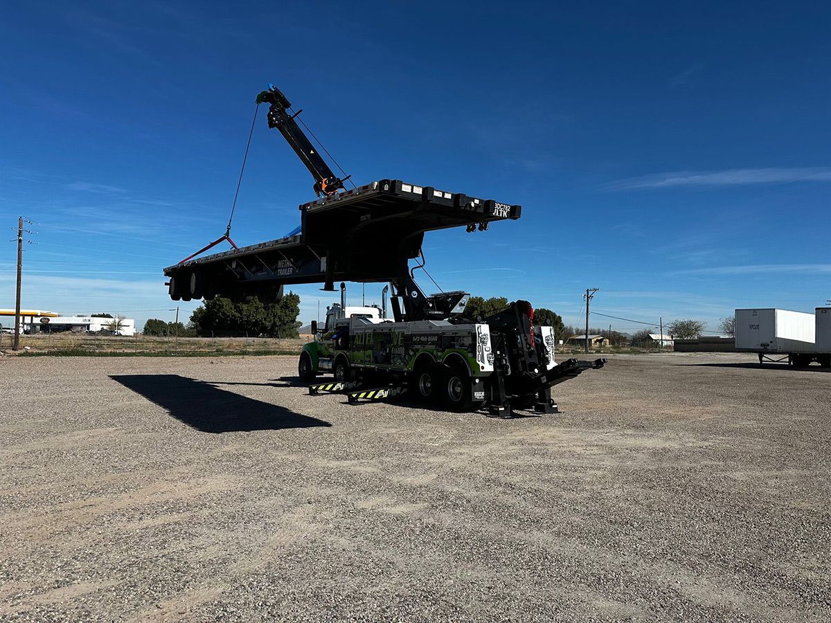 A large piece of metal is being lifted by a crane in a gravel lot.