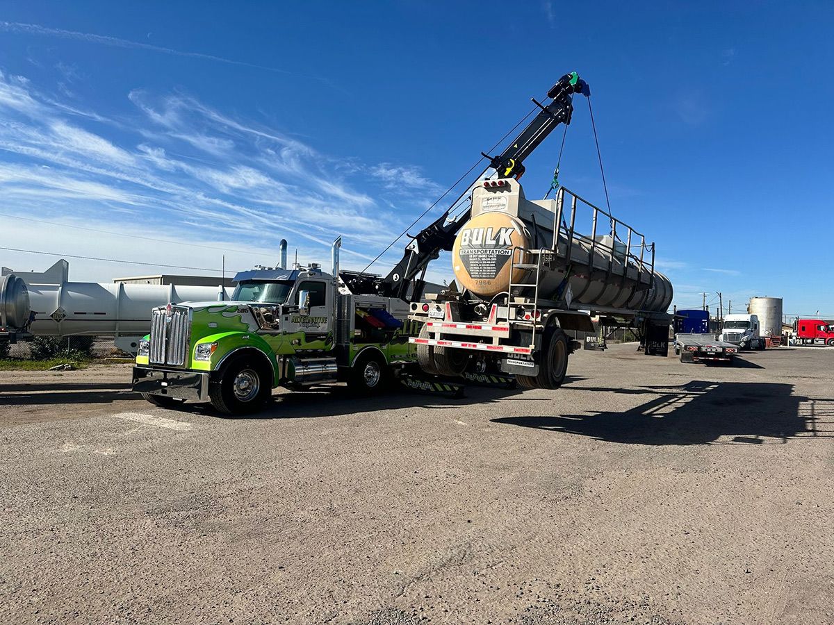 A truck is being towed by a crane in a gravel lot.