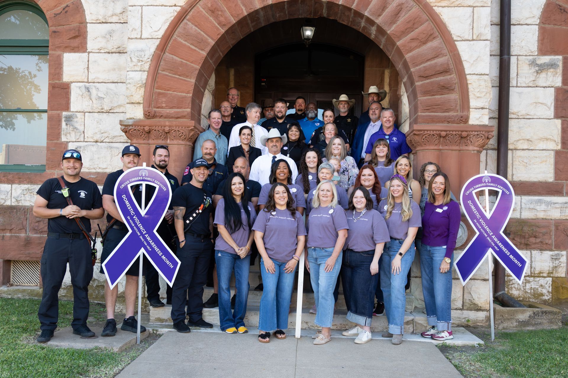 Group of people outside a building, many wearing purple, holding purple awareness ribbons.