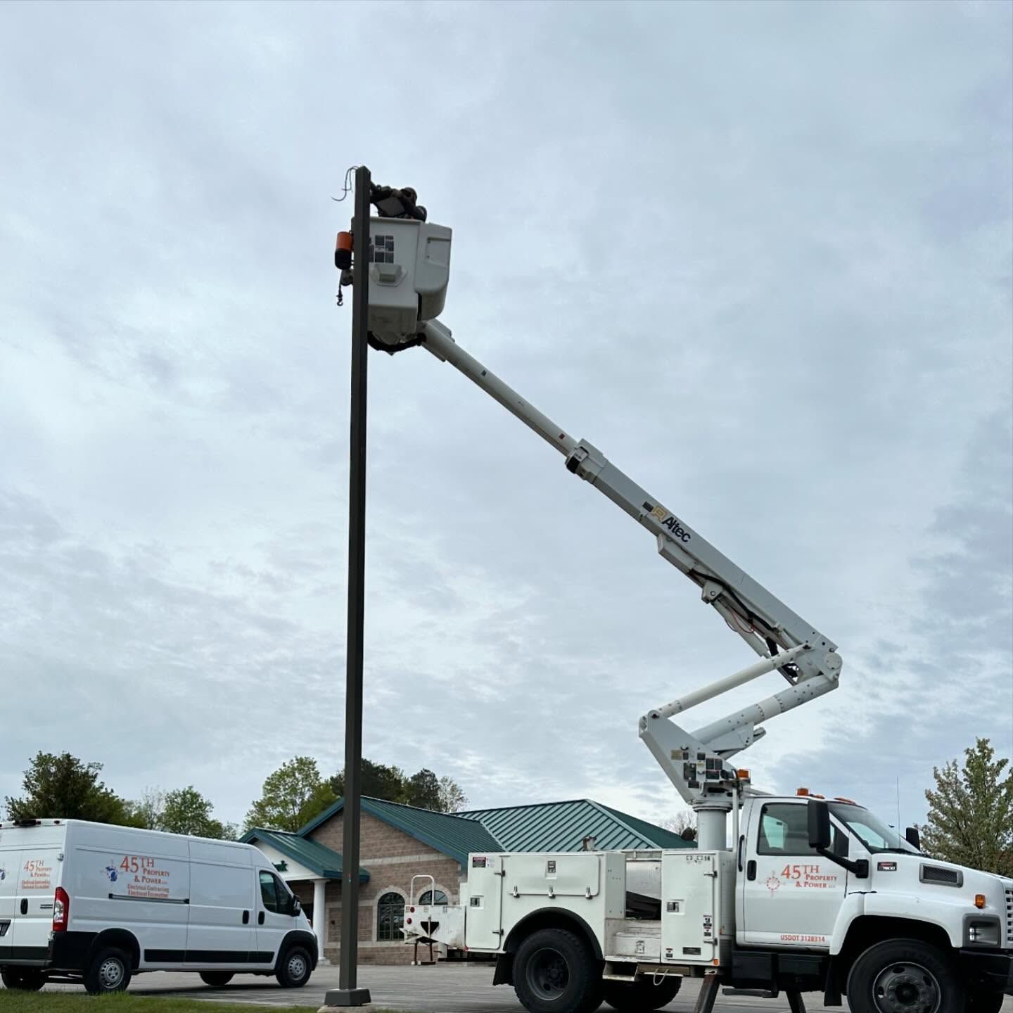 Truck with extended arm reaching a street light under cloudy skies.