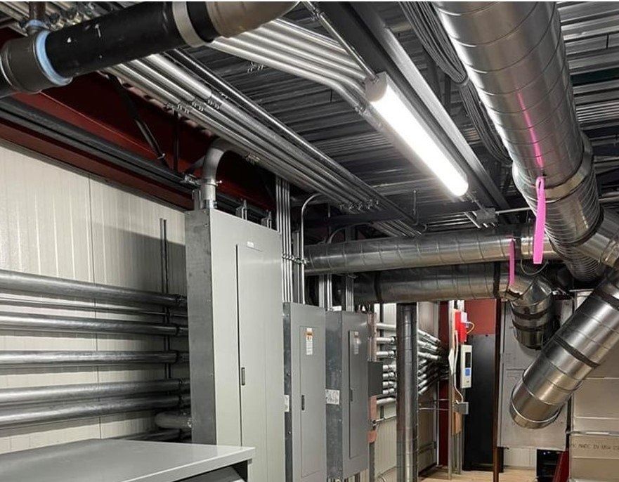 Electrical conduit and ductwork in a commercial building, with gray metal panels, a fluorescent light, and white walls.