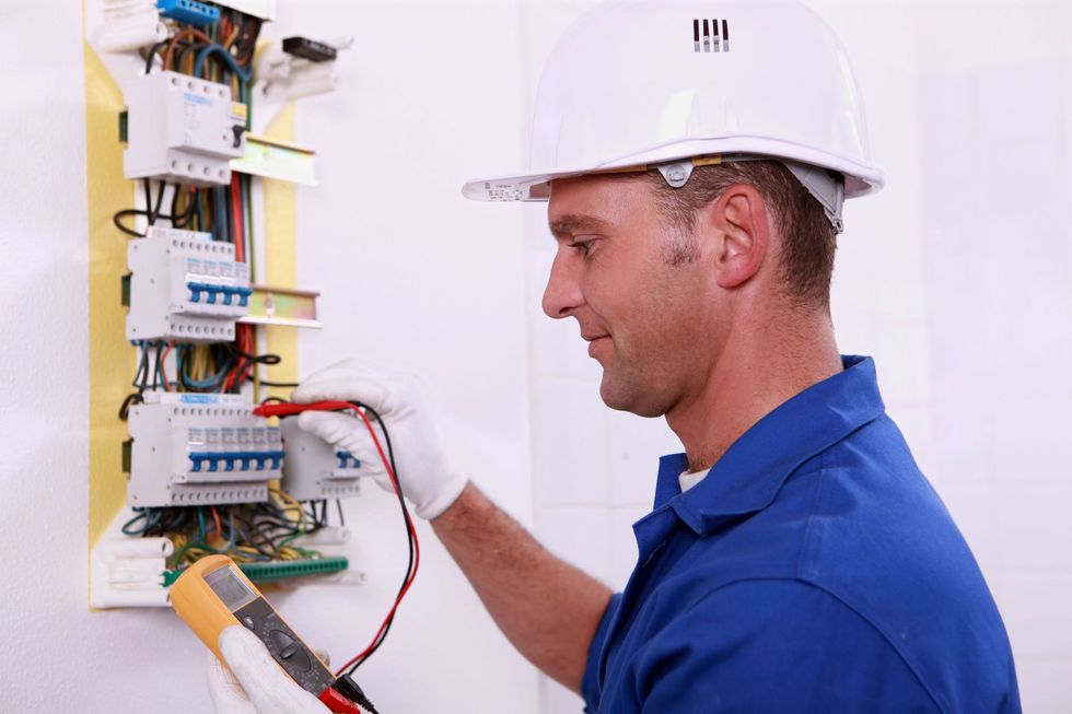 Electrician installing a wall outlet, using a screwdriver, indoors.
