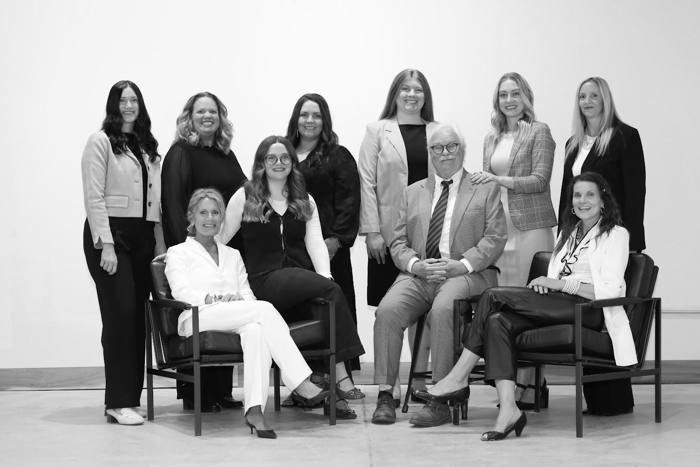 Group of nine people posing in a studio, seated and standing in black-and-white attire