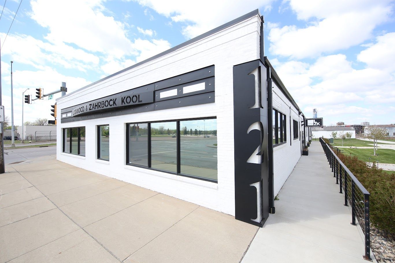 Modern white-and-black commercial building with large windows on a sidewalk under a partly cloudy sky