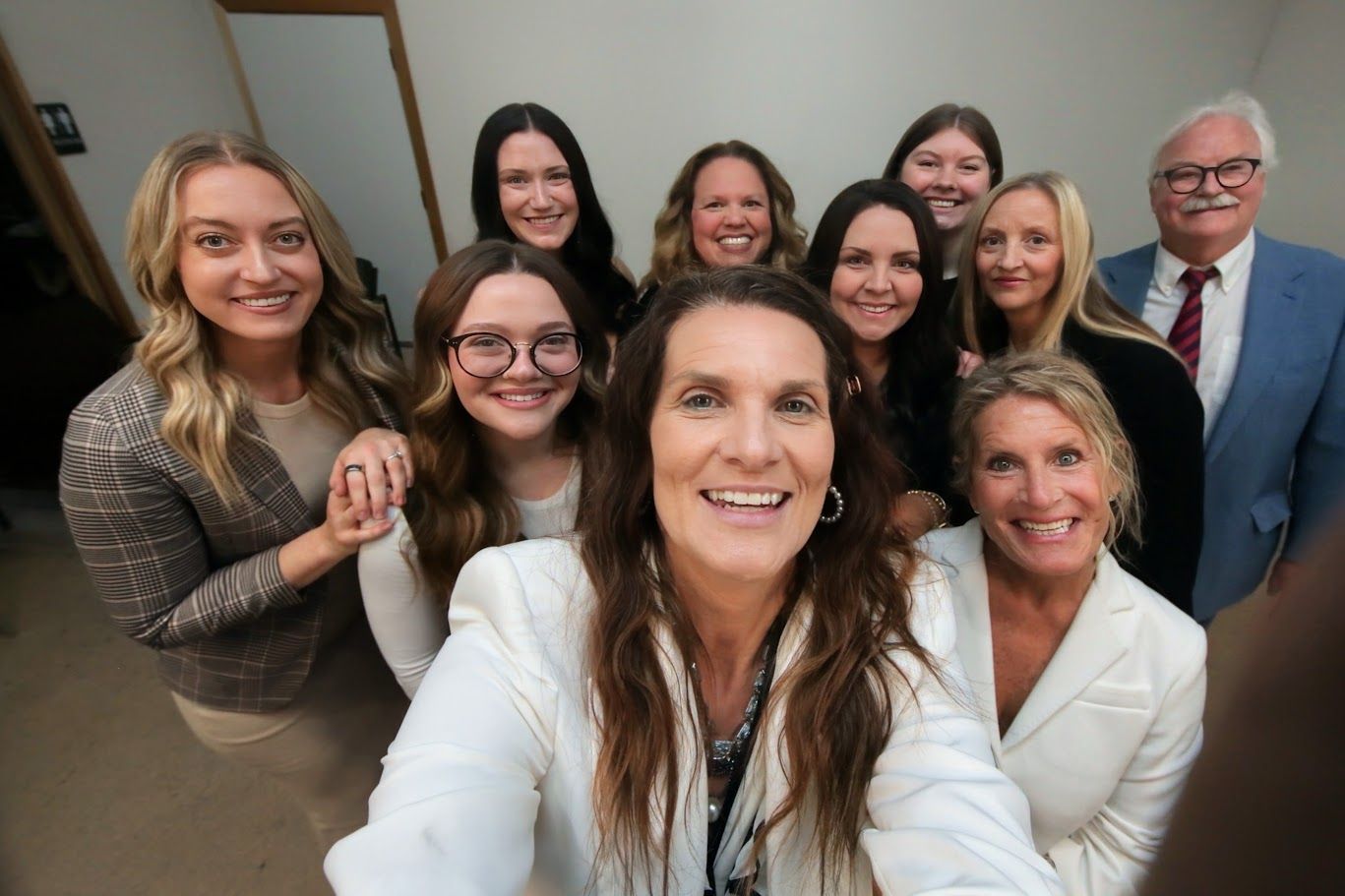 Group selfie of eight smiling people in business attire indoors