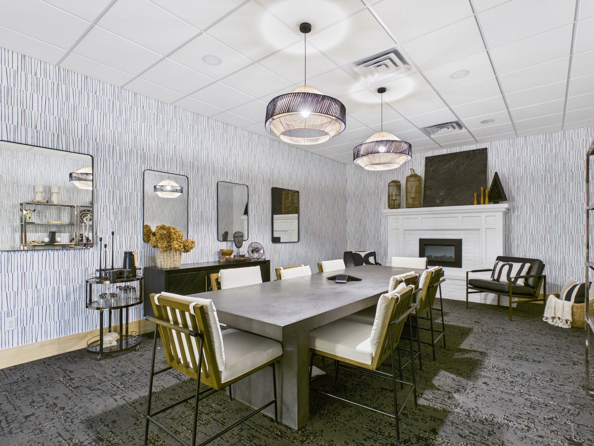 A modern dining room features a long rectangular table, upholstered chairs, two pendant lights, and a fireplace.