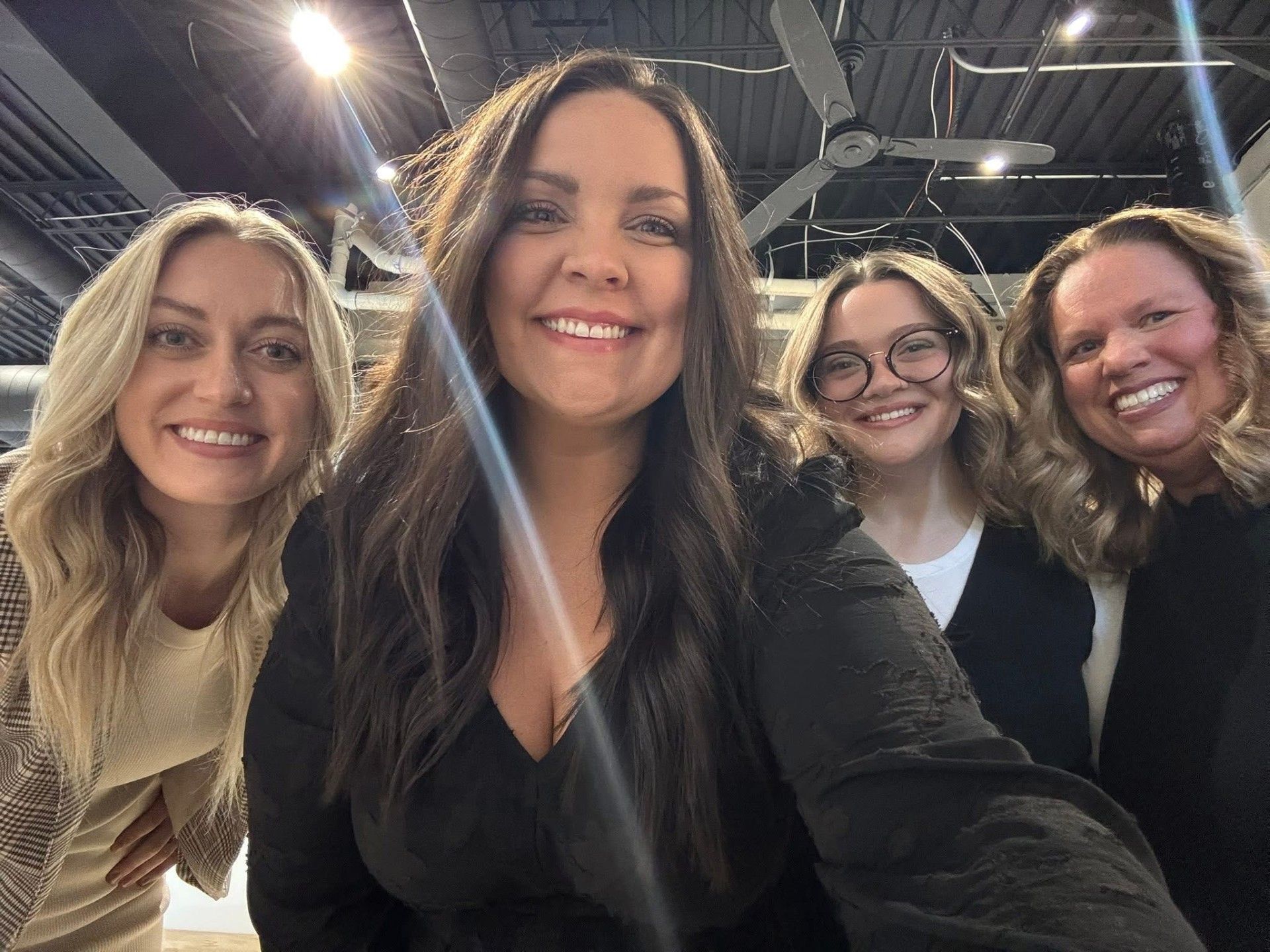 Four smiling people posing for a selfie in a bright indoor space with ceiling lights