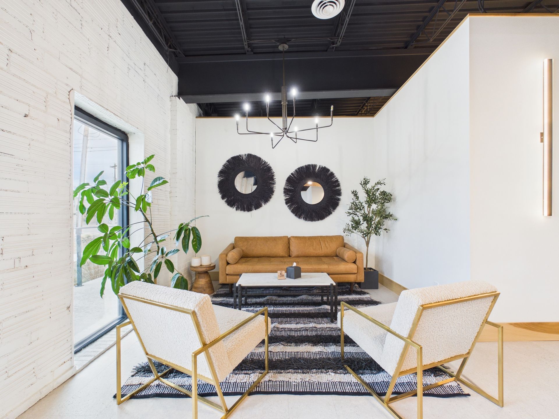 Modern lobby with a tan leather sofa, two cream armchairs, a geometric rug, two round mirrors, and a black ceiling.