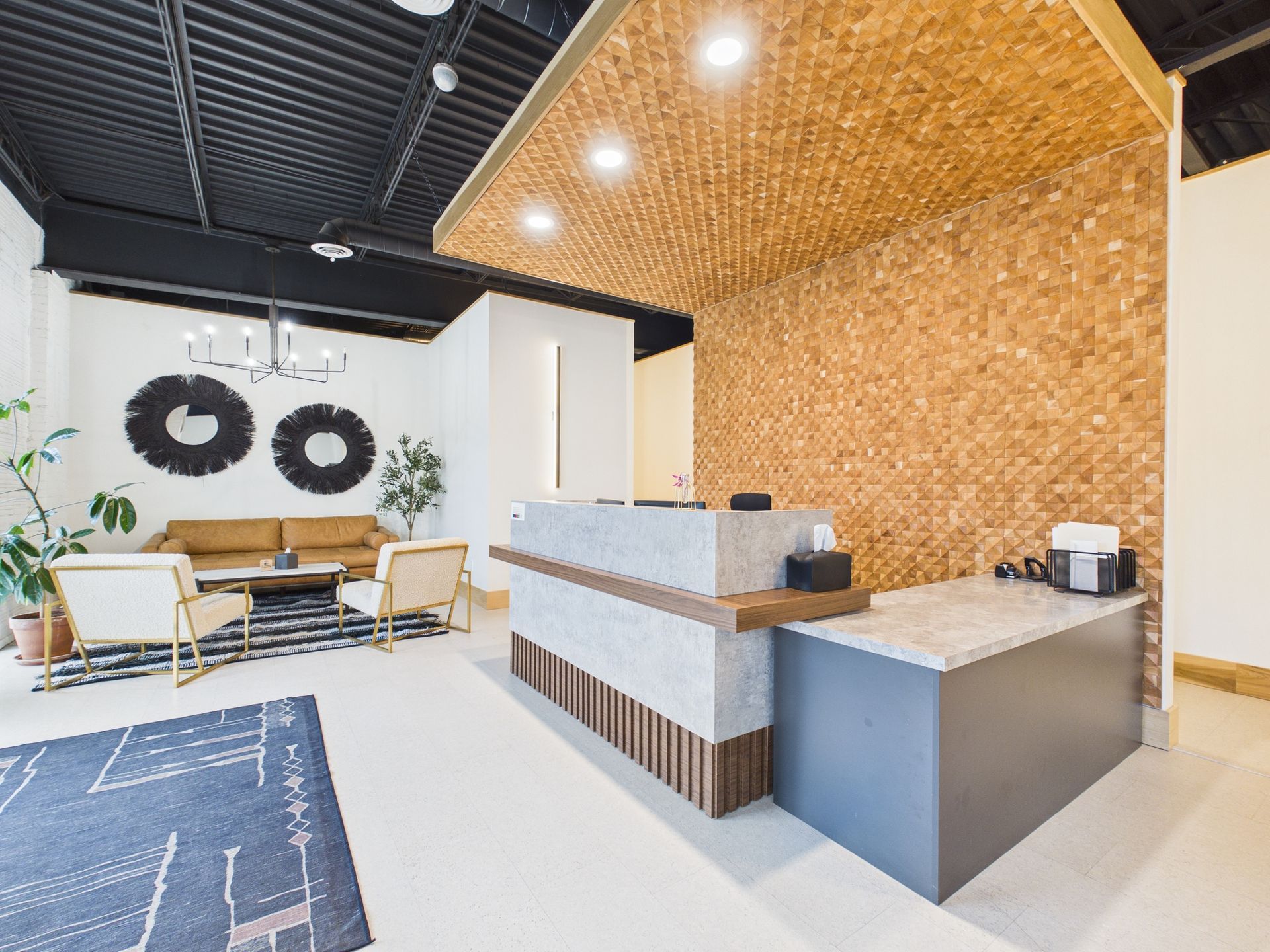A modern reception area featuring a concrete desk, textured wood canopy, black ceiling, and a seating area with a sofa.