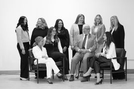 Group of people seated and standing in a studio portrait, smiling in light and dark outfits.