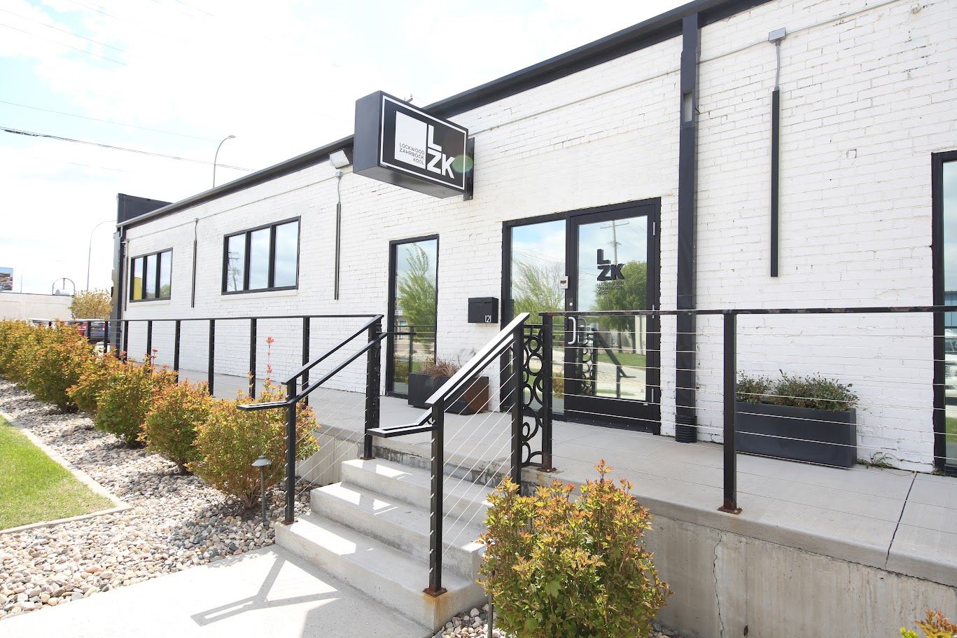 Modern white building with black trim, front steps, and landscaped walkway under bright daylight