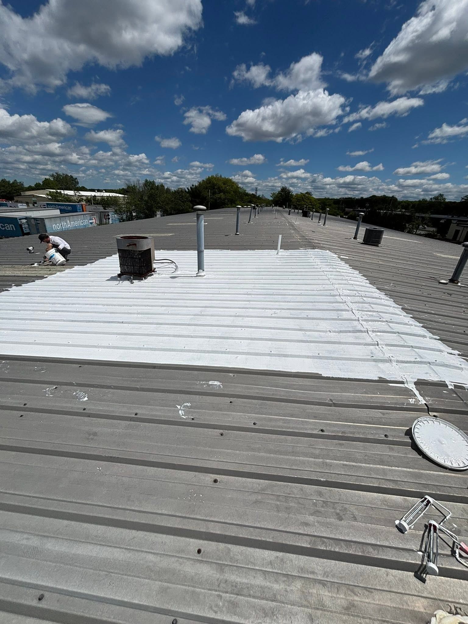 Rooftop with white roofing membrane, gray gravel edge, vents, and blue sky with clouds.
