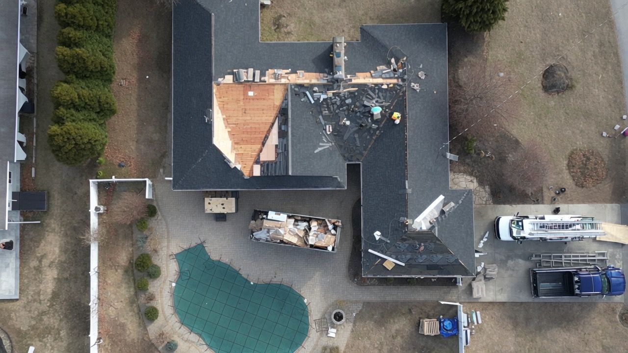 Aerial view of a house roof under construction, with materials, a truck, and a swimming pool nearby.