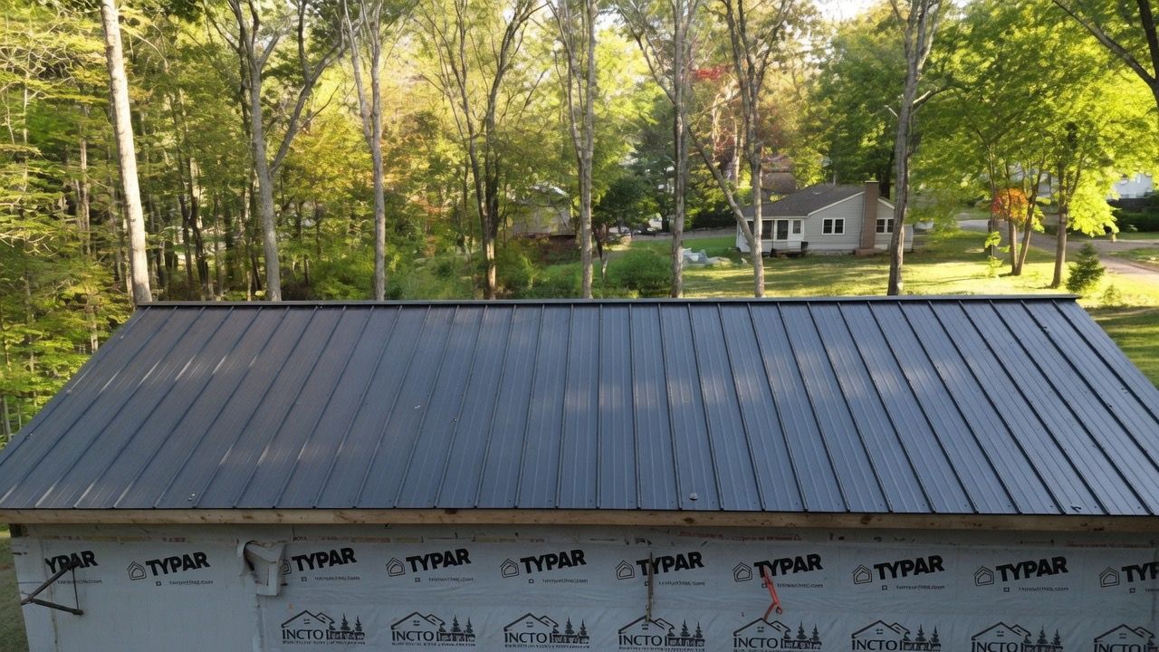 Roof under construction with gray shingles, trees in back, and a house across the yard.
