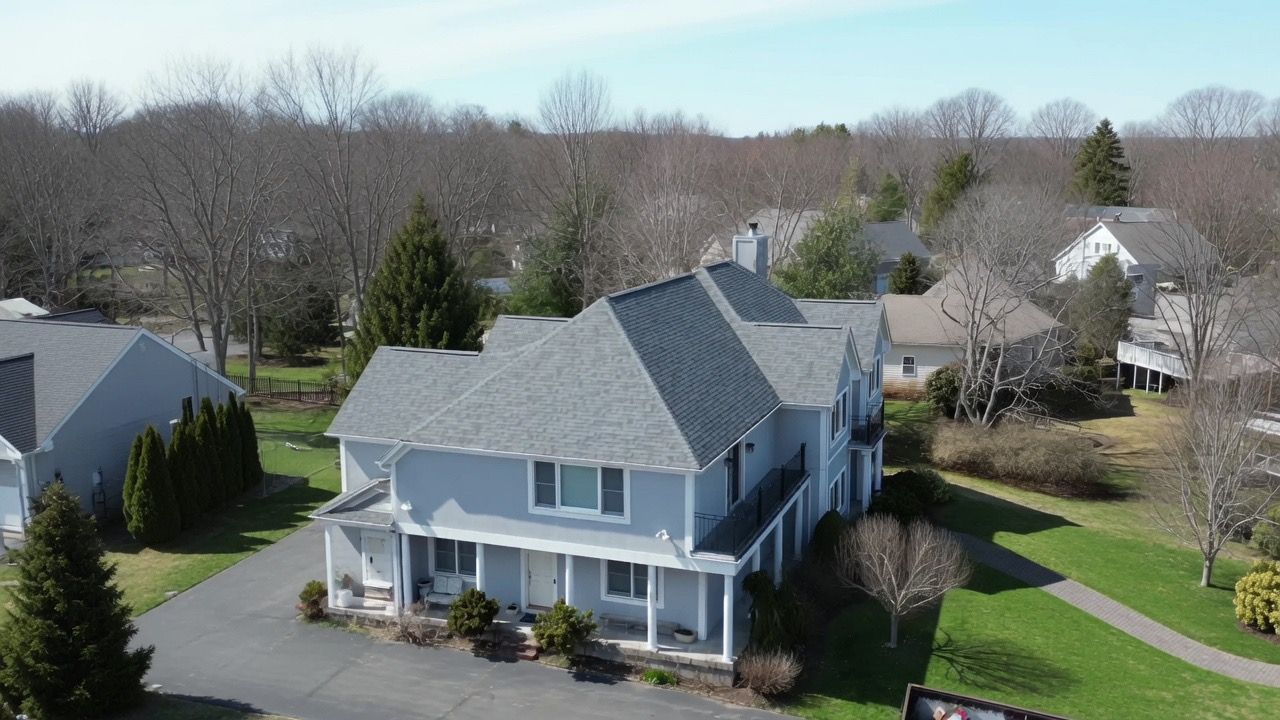 Blue two-story suburban house with a front porch, driveway, and surrounding trees on a sunny day