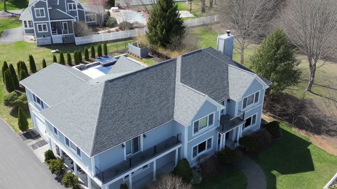 Aerial view of a large gray house with a dark roof and surrounding trees and lawn.