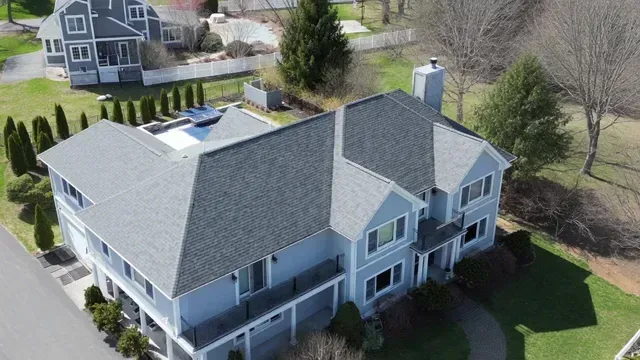 Aerial view of a large gray two-story house with a landscaped yard and neighboring homes nearby.