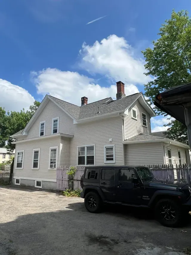 White house with ornate trim under a blue sky, with a black Jeep parked in front