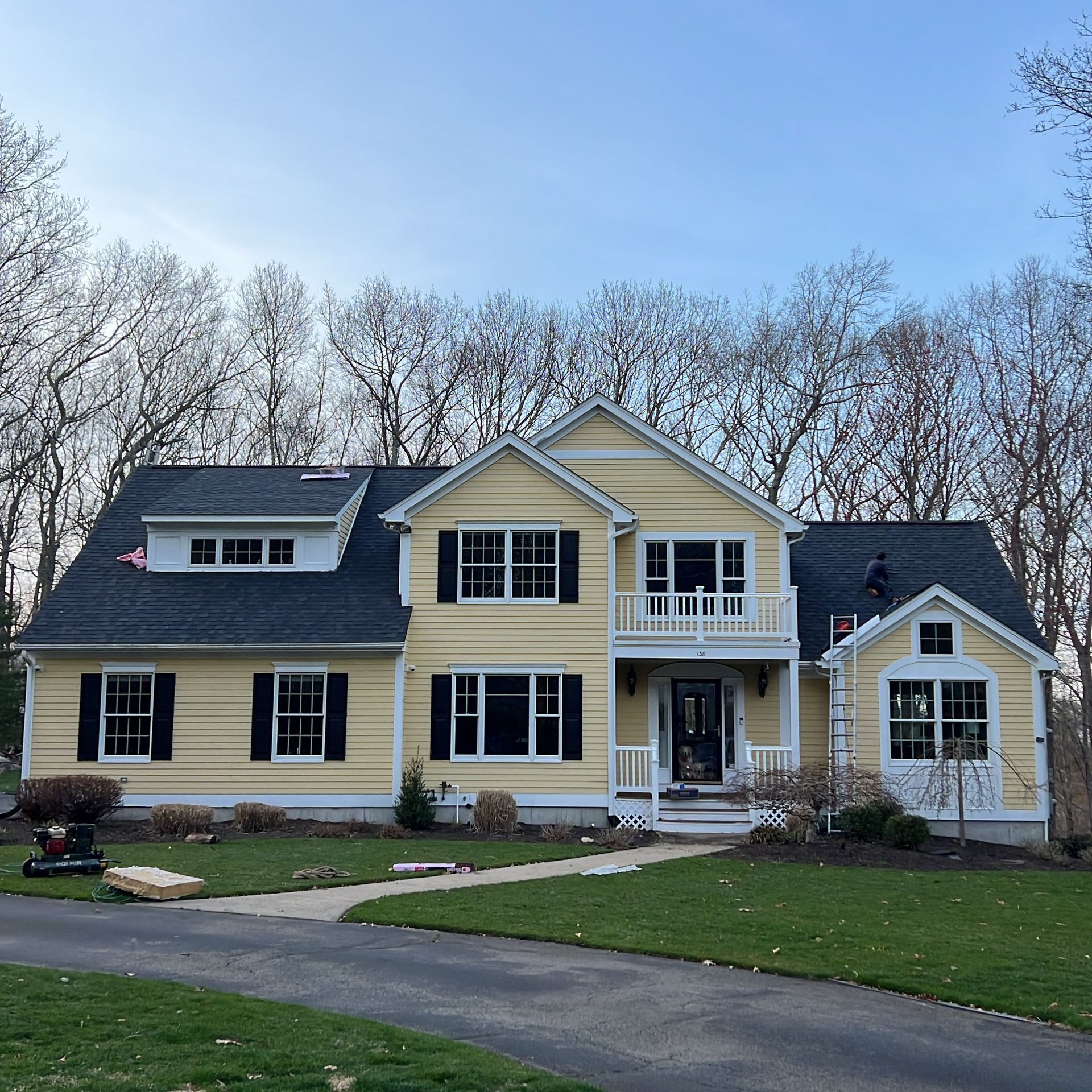 Large yellow two-story house with black shutters, front porch, balcony, and curved driveway