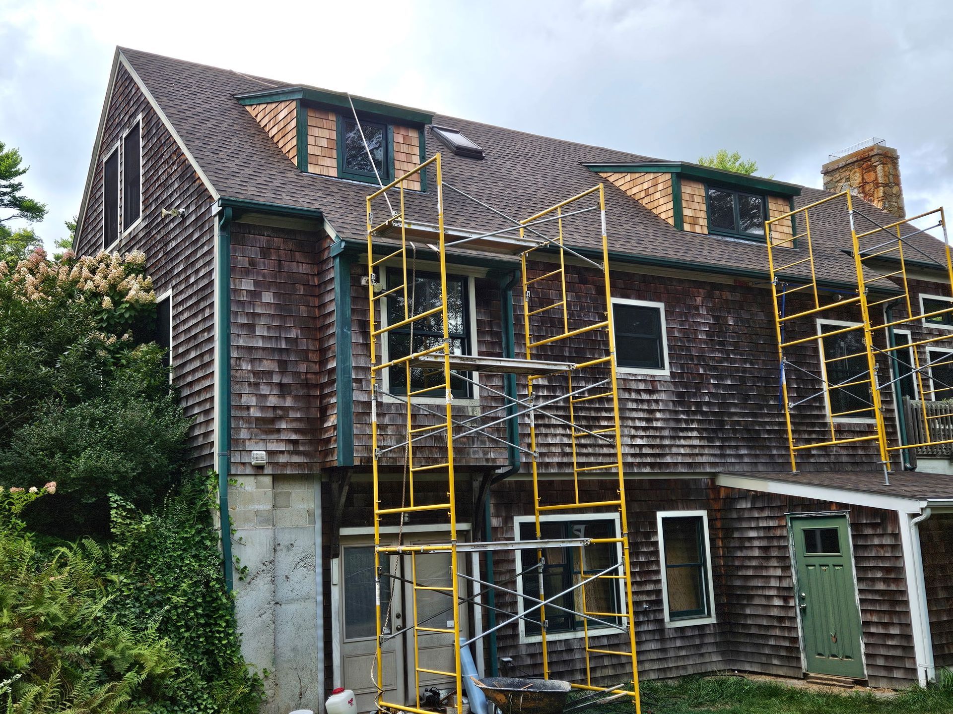Old house with yellow scaffolding during exterior repair, shingled roof and weathered siding