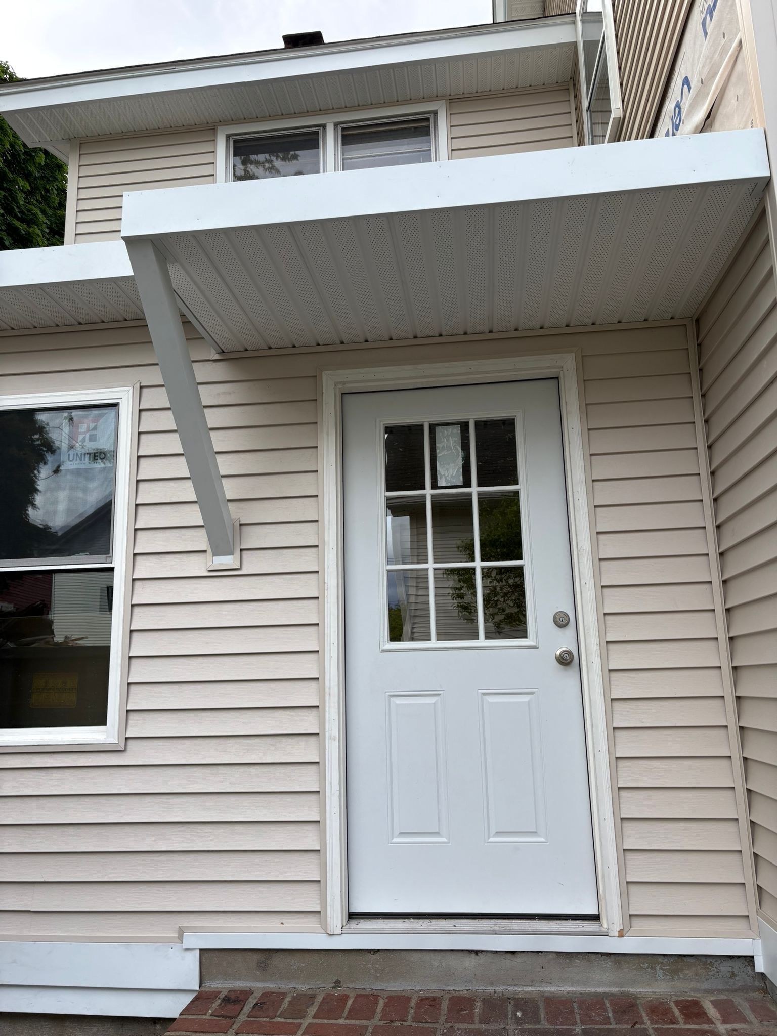 White front door under a small awning on a beige-sided house with a window beside it.