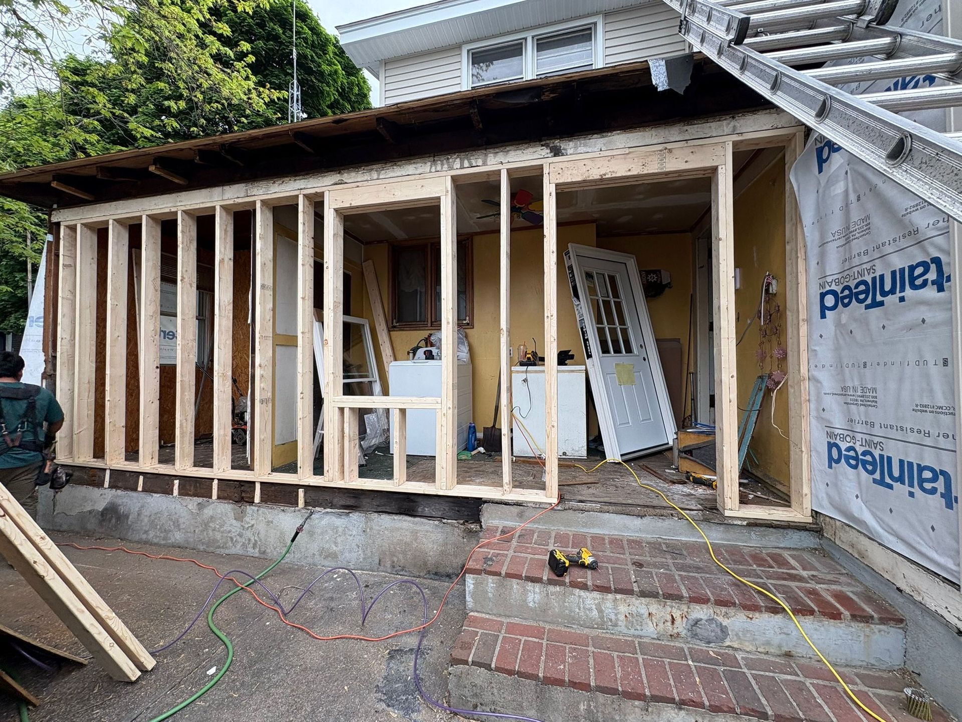 Partially framed house exterior with exposed wood studs and construction materials on the ground