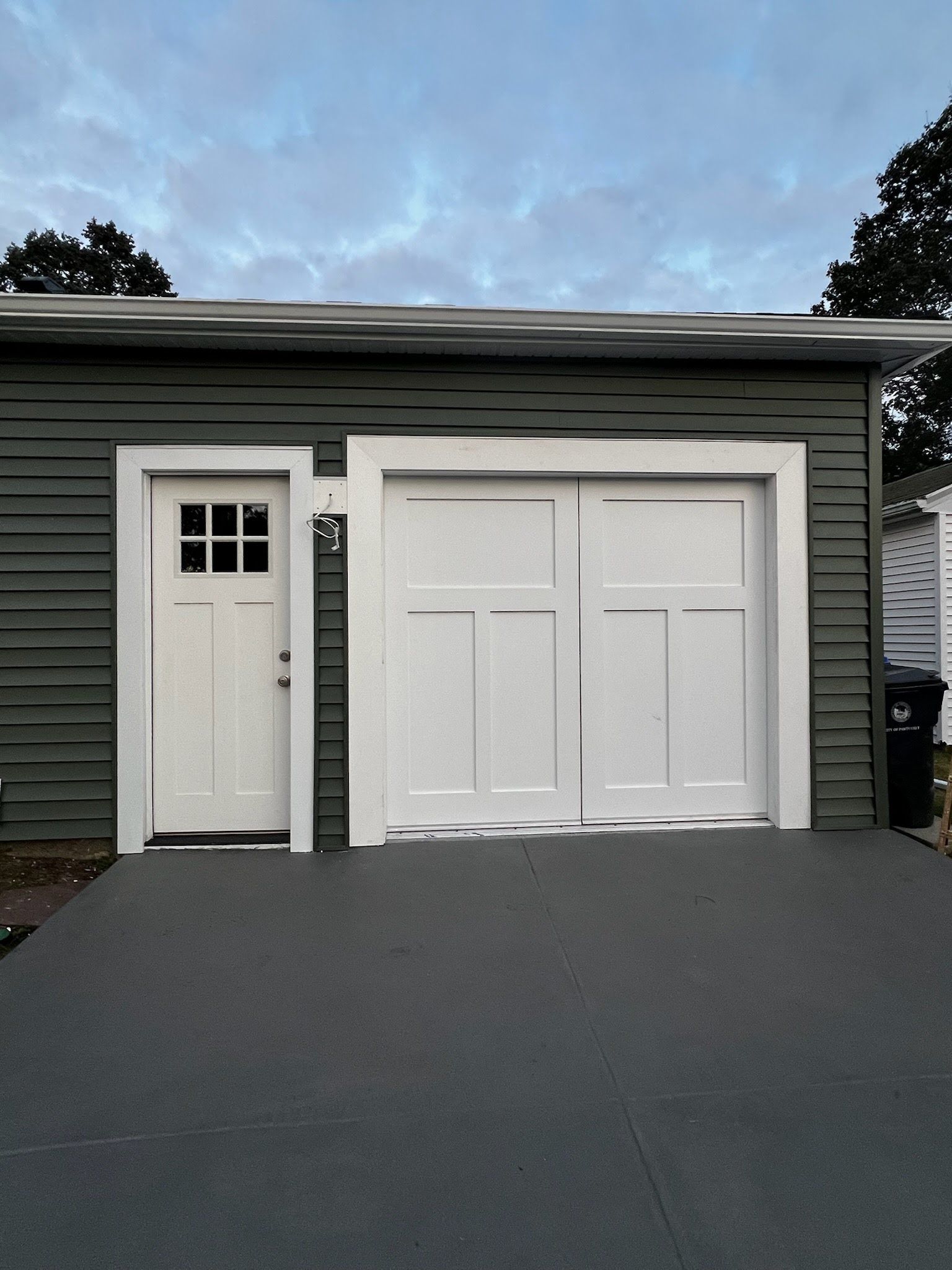 White garage door and side entry door on a gray building at dusk