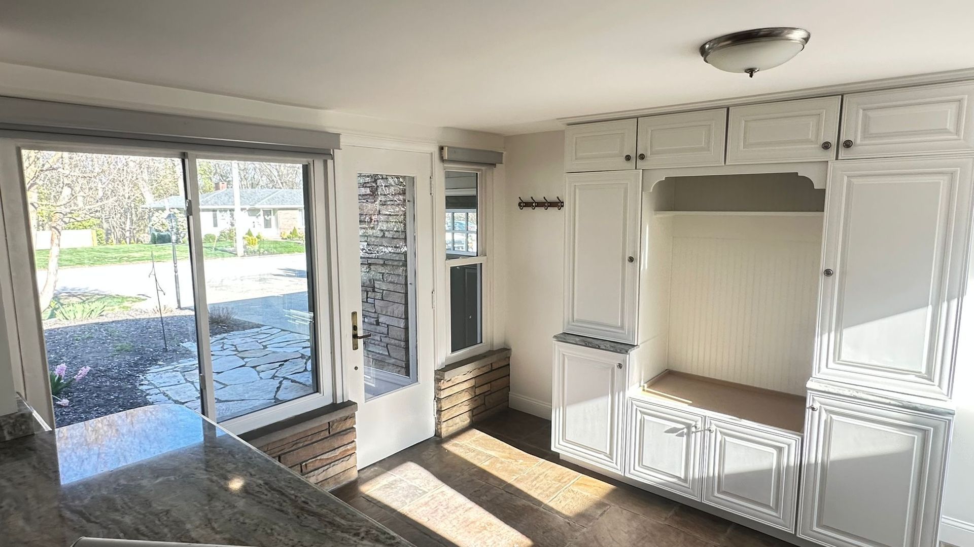 Bright room with sliding glass doors, sunlight, and a white built-in cabinet wall with bench seating.
