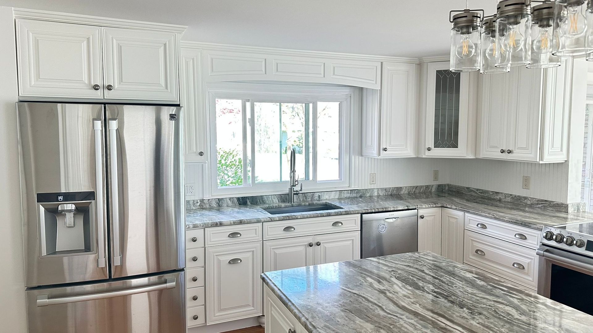 Bright white kitchen with stainless steel appliances, marble island, and large window over the sink