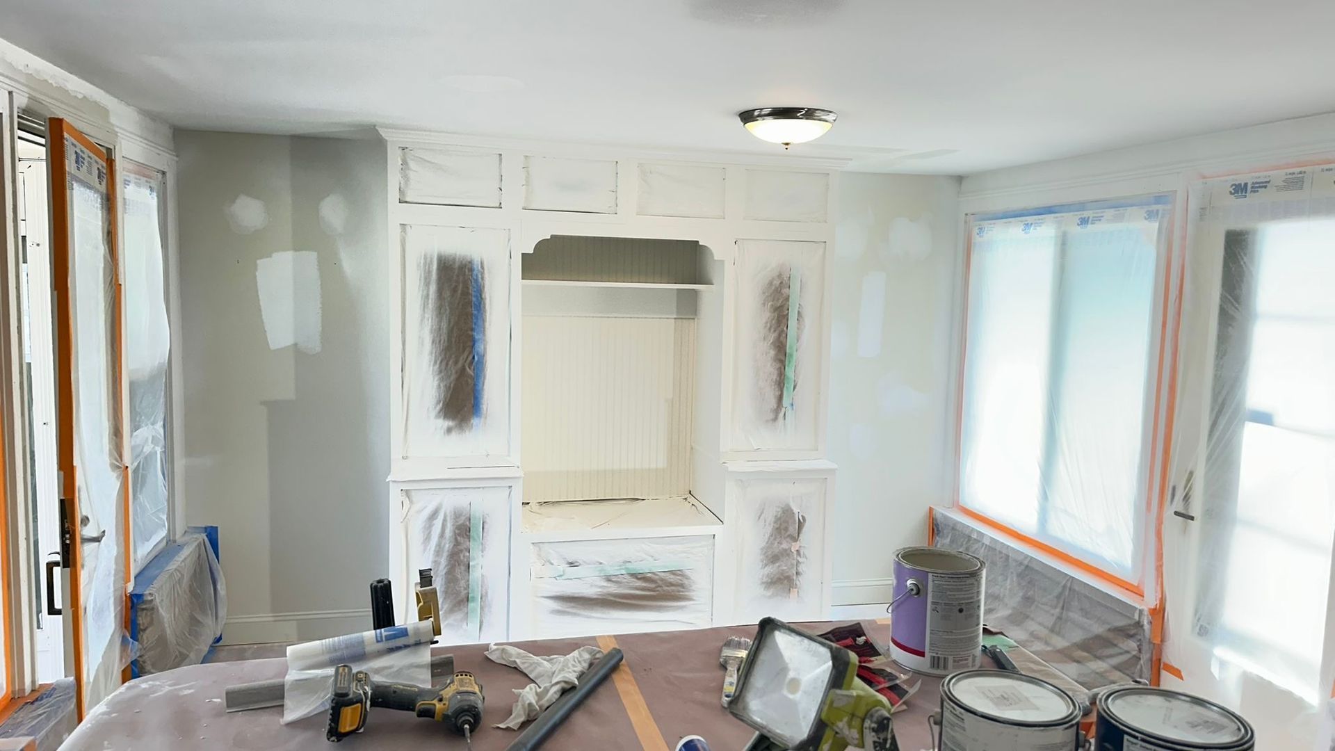 Renovated living room with white cabinets, fresh drywall, and construction tools on the floor