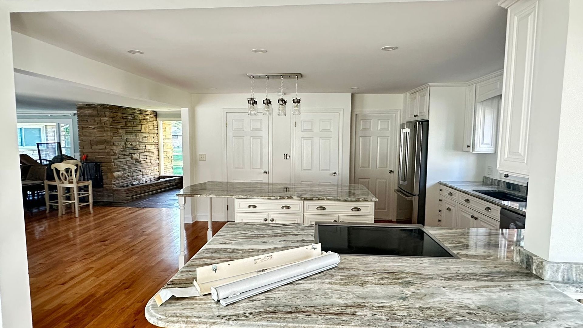 Modern kitchen with granite island, white cabinets, stainless fridge, and hardwood floors leading to dining area