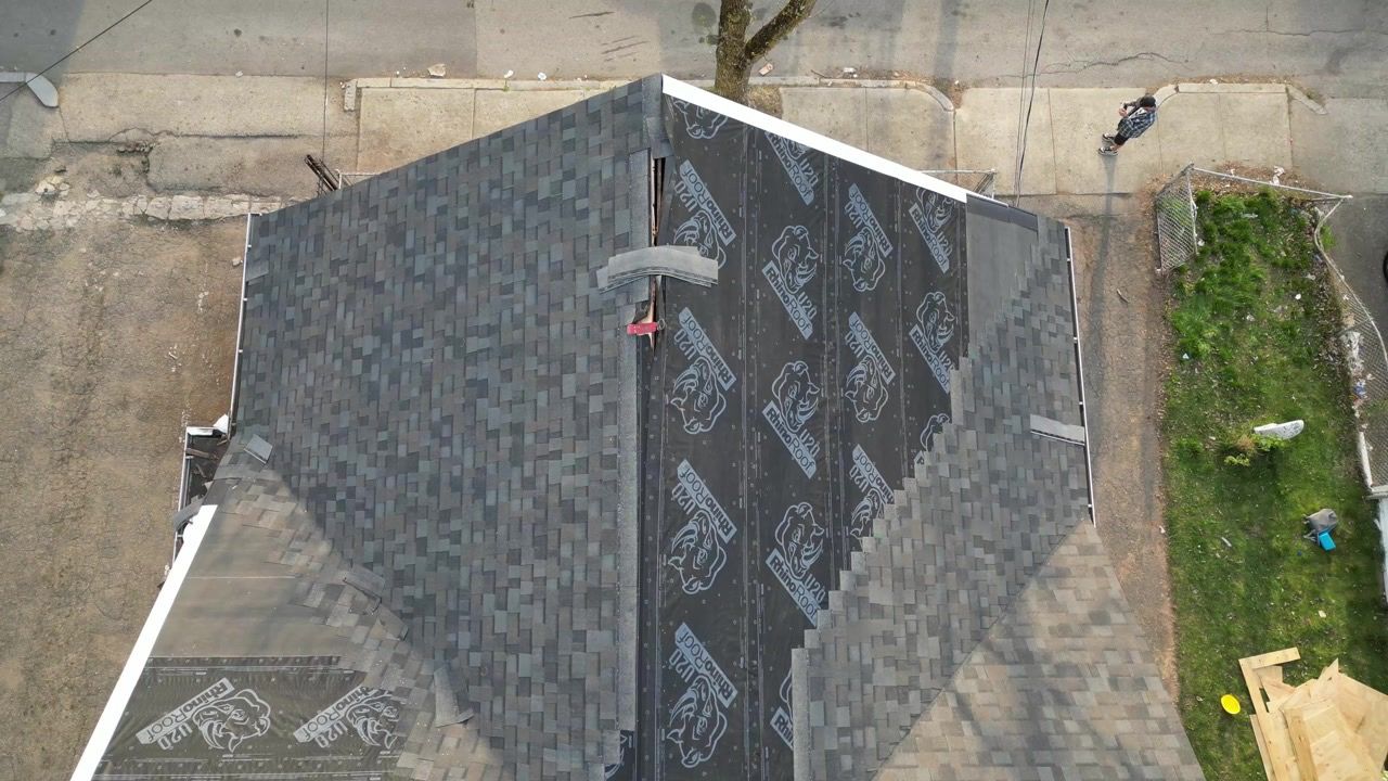 Aerial view of a gray shingled roof with a vent pipe, bordered by concrete and grass.