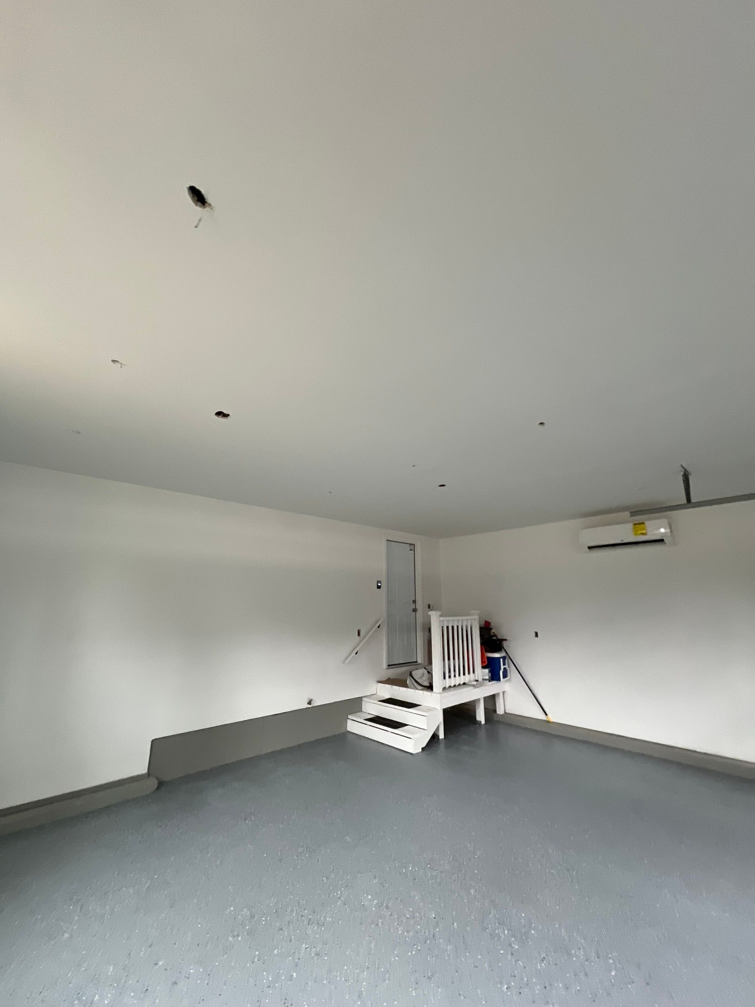 Empty garage with white walls and ceiling, gray floor, and a small step stool near the back wall.