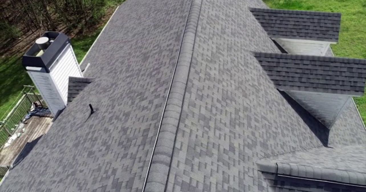 Aerial view of a gray shingled house roof with dormers and a chimney.