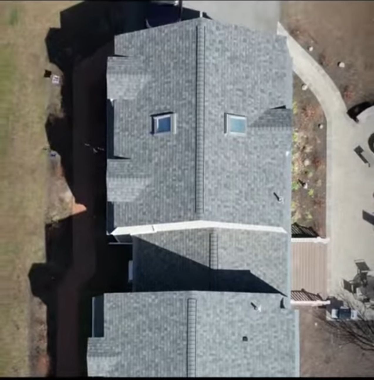 Aerial view of two gray-shingled house roofs with skylights and a driveway beside them.