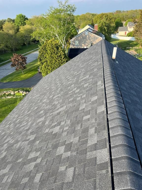 Gray shingled roof with ridge vent, viewed from above over a suburban neighborhood and trees