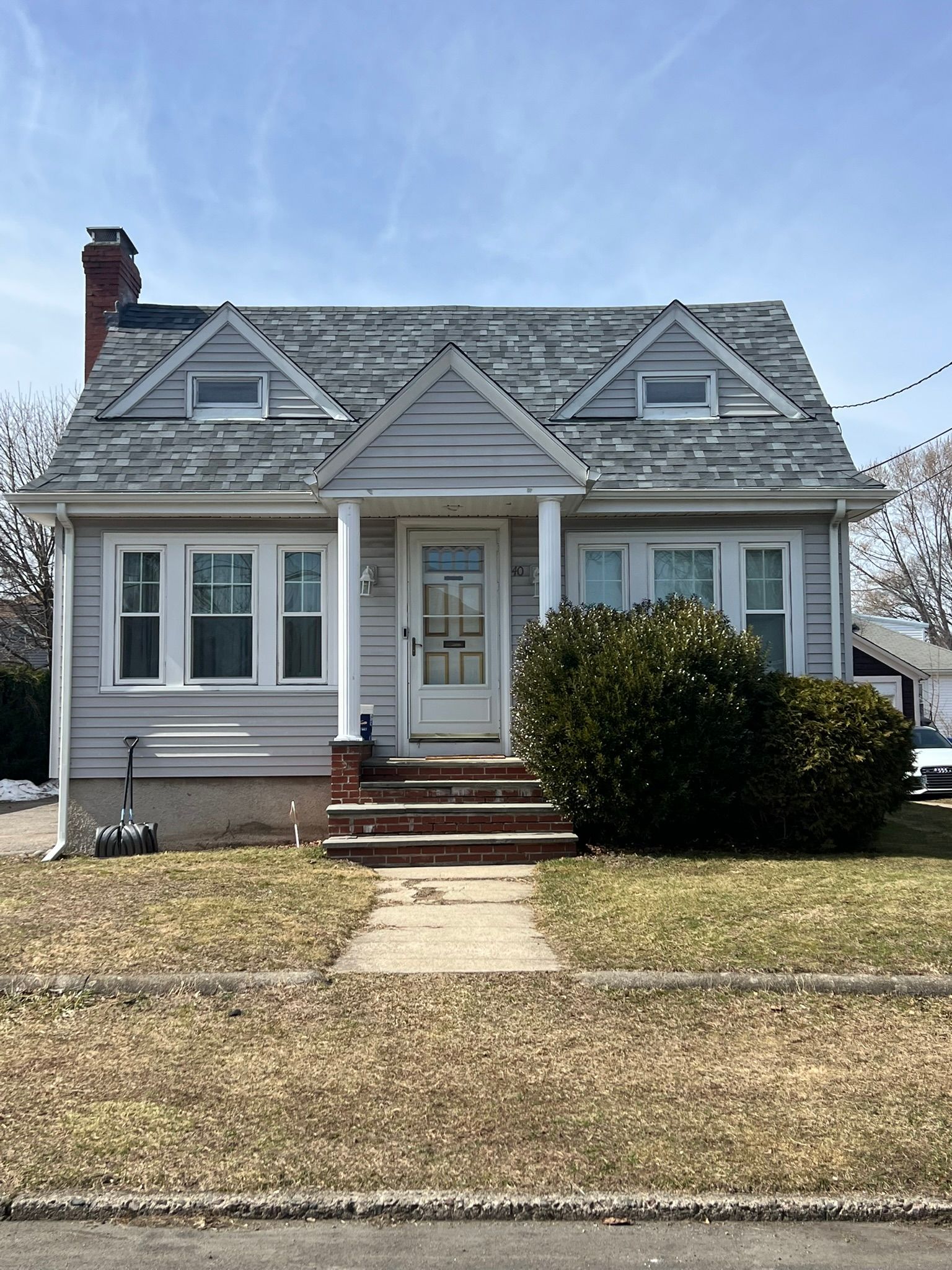 Small gray house with white trim, front steps, and a porch in a suburban yard.