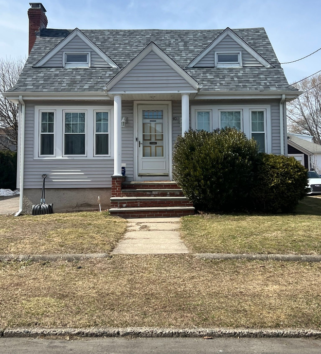 Small gray house with white trim, front porch, and brick steps behind a lawn and sidewalk.