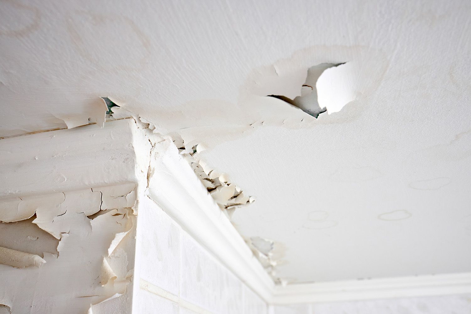 Peeling white ceiling paint and water damage above a doorway