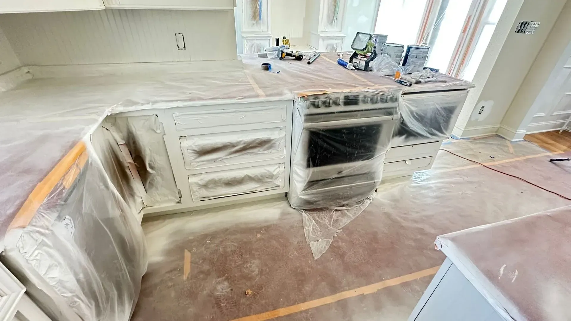 Kitchen cabinets and island wrapped in plastic during home renovation, with countertops and floor protected.