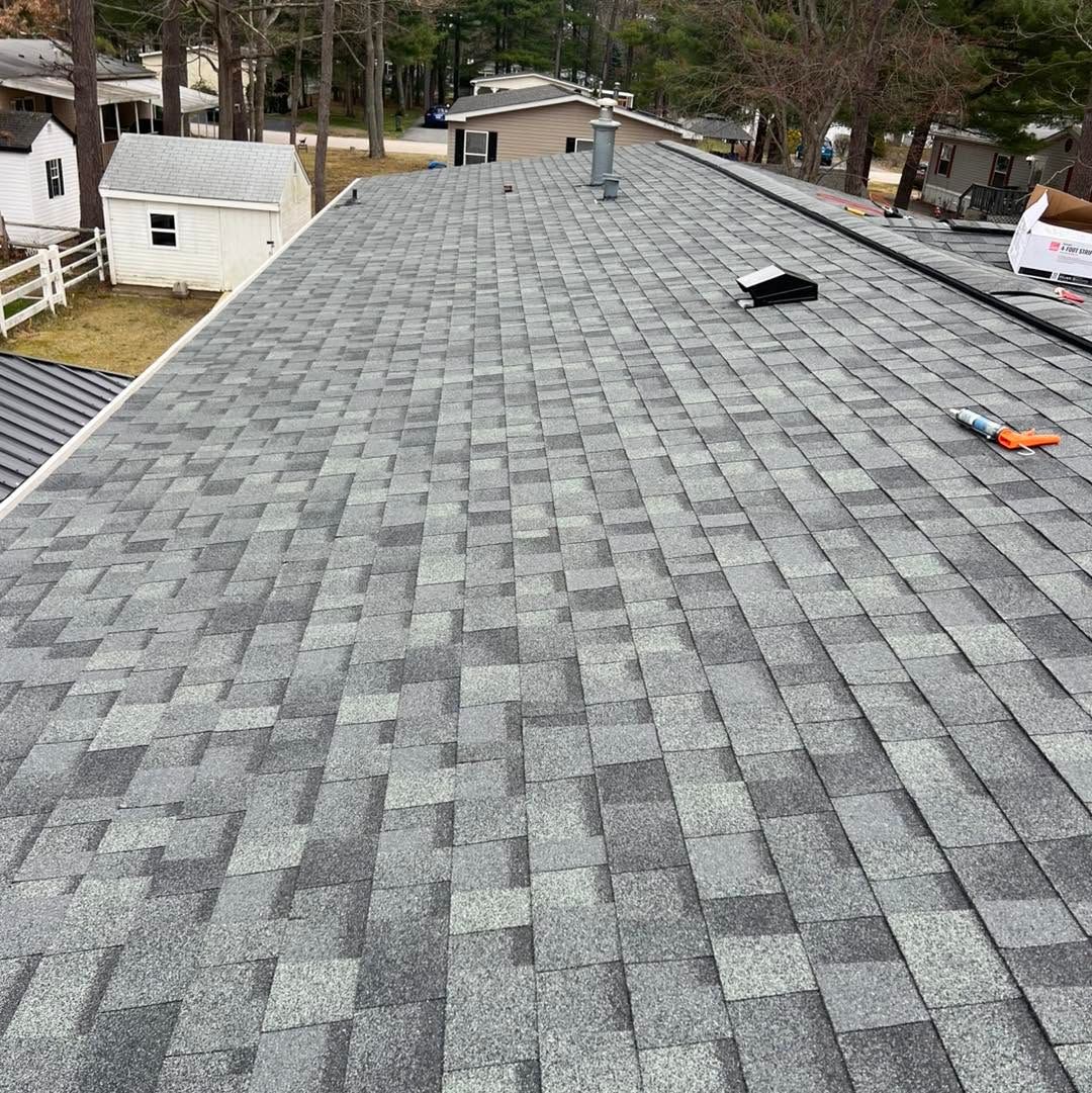 Gray shingled roof seen from above, with tools and a white shed in the background.