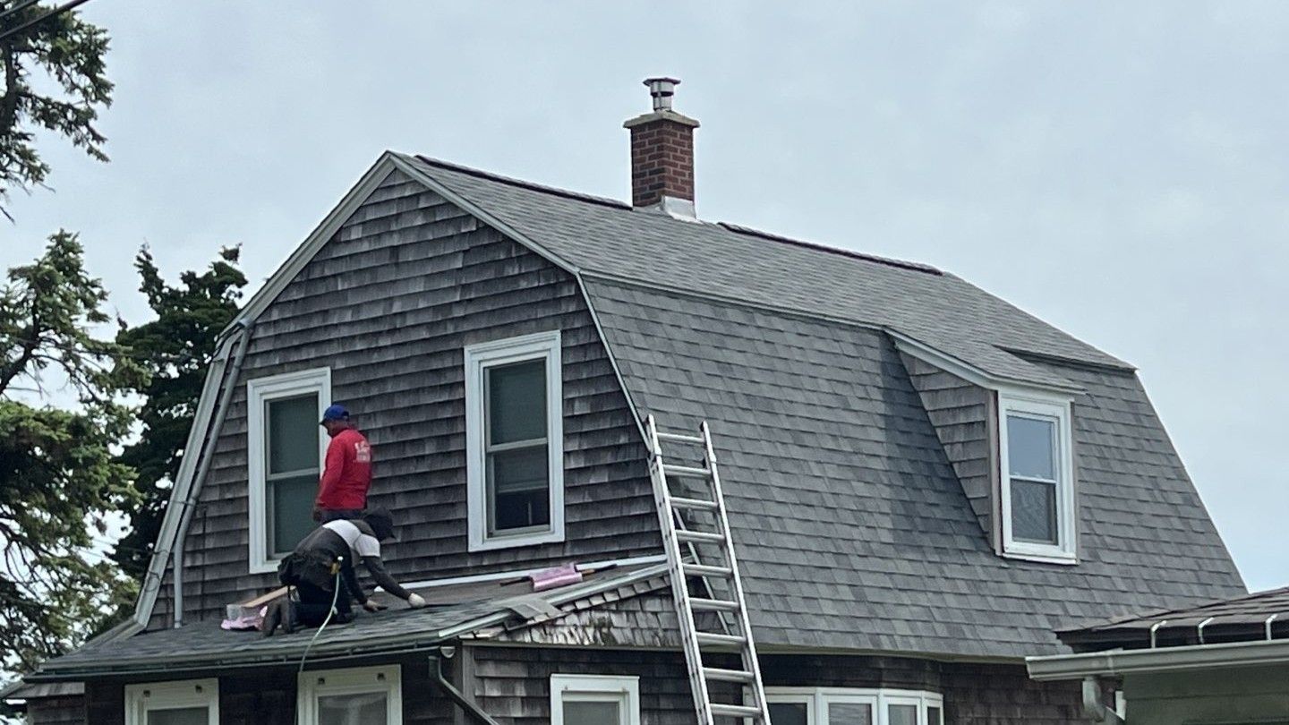Worker on a ladder repairing a gray shingled roof on a house