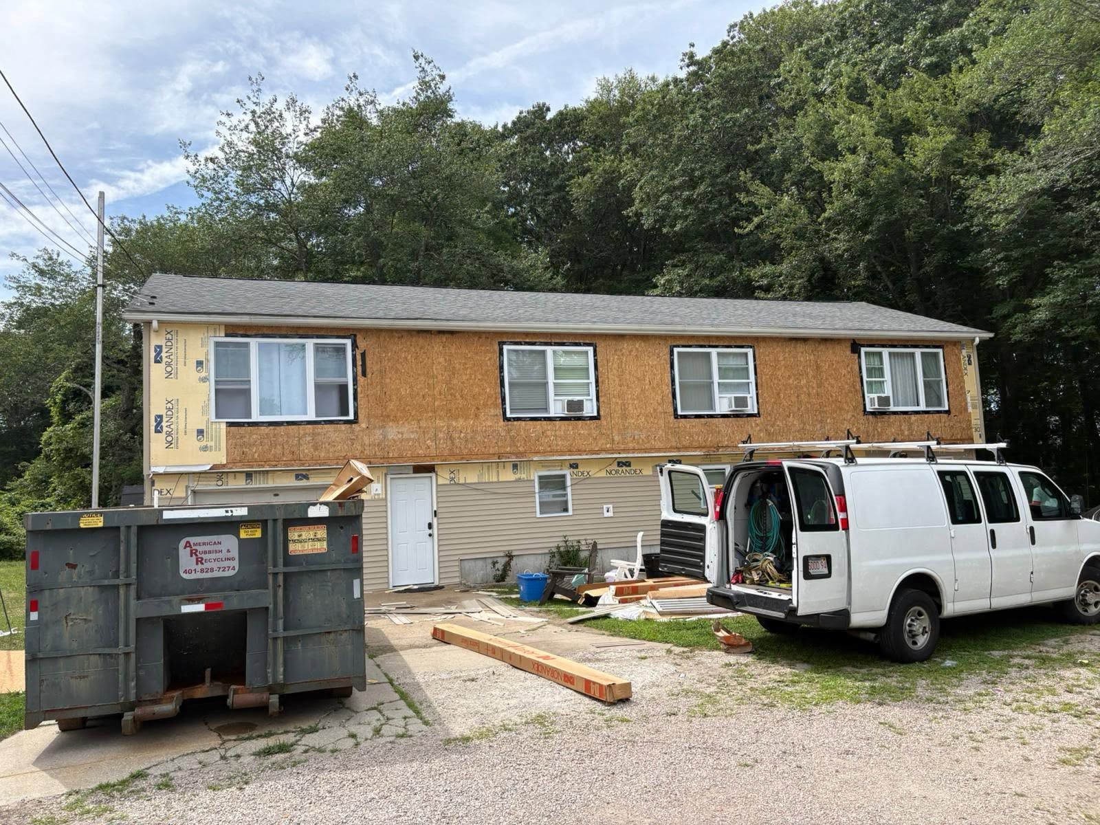 Two-story house under renovation with a white work van, dumpster, and construction debris in front