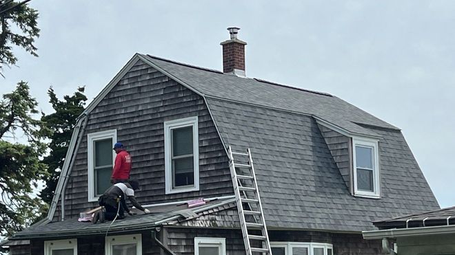 Worker on a ladder repairing a gray shingled roof on a house