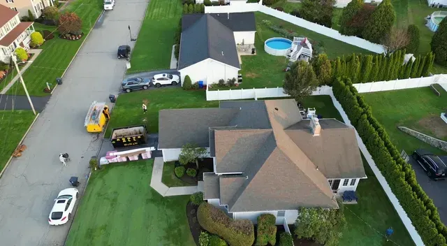 Aerial view of a suburban home with a driveway, parked cars, and a swimming pool in the backyard