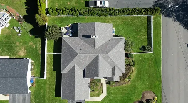 Aerial view of a gray-roofed house with a green lawn and nearby street.