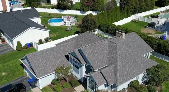 Aerial view of a suburban house with a gray shingled roof and backyard pool