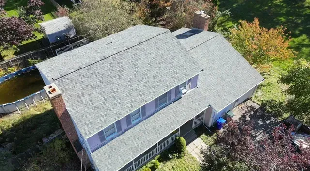 Aerial view of a gray-roofed house surrounded by trees and yard greenery