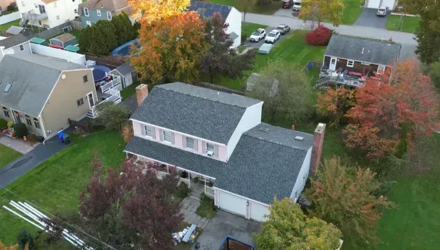 Aerial view of a suburban house with gray roof, pink siding, and autumn trees around it.